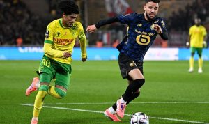 Dua pemain sepak bola, satu dari Nantes (kuning-hijau) dan satu dari Lille (biru gelap), berduel memperebutkan bola di lapangan hijau.