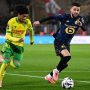 Dua pemain sepak bola, satu dari Nantes (kuning-hijau) dan satu dari Lille (biru gelap), berduel memperebutkan bola di lapangan hijau.