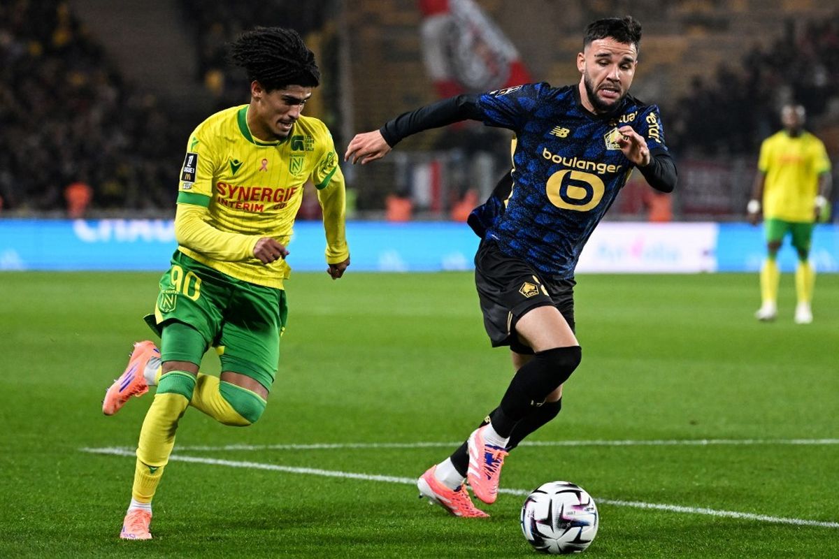 Dua pemain sepak bola, satu dari Nantes (kuning-hijau) dan satu dari Lille (biru gelap), berduel memperebutkan bola di lapangan hijau.