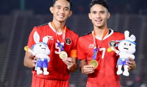 Timnas-U22-Indonesia-Emas-SEA-Games-Pemain-Bangga.webp Dua pemain Timnas U-22 Indonesia mengenakan medali emas SEA Games dan memegang maskot, tersenyum bangga di lapangan.