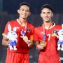 Dua pemain Timnas U-22 Indonesia mengenakan medali emas SEA Games dan memegang maskot, tersenyum bangga di lapangan.
