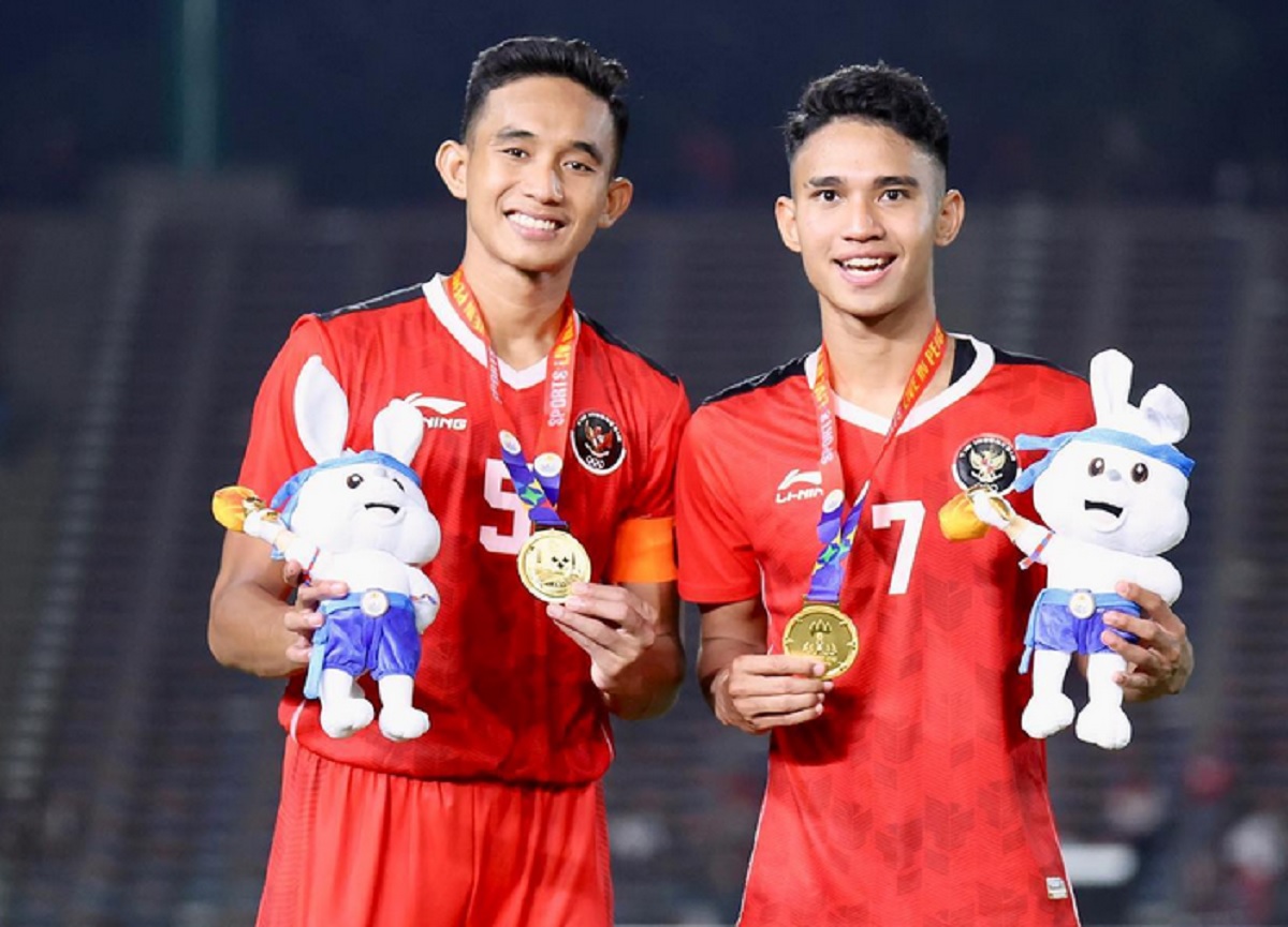 Timnas-U22-Indonesia-Emas-SEA-Games-Pemain-Bangga.webp Dua pemain Timnas U-22 Indonesia mengenakan medali emas SEA Games dan memegang maskot, tersenyum bangga di lapangan.