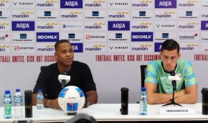 Patrick Kluivert dan Jay Idzes kapten Timnas Indonesia di konferensi pers, dengan bola sepak Molten di meja dan spanduk sponsor di latar belakang.