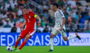 Pemain Timnas Indonesia bernomor punggung 3, Jay Idzes berseragam merah menggiring bola di lapangan, dibayangi oleh pemain Timnas Arab Saudi berseragam putih