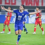 Persib-Bandung-Rayakan-Gol-Fase-Gugur-AFC-Champions-League-2.webp Pemain Persib Bandung, mengenakan seragam biru dengan nomor 90, merayakan gol dengan tangan terentang di lapangan.