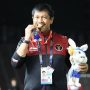 Pelatih Indra Sjafri tersenyum gembira sambil menggigit medali emas dan memegang boneka maskot kelinci, mengenakan jaket tim nasional Indonesia di stadion