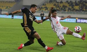 Dewa-United-AFC-Challenge-League-Seri-Klub-Kamboja.webp Pemain Dewa United (seragam hitam-emas) berduel ketat dengan pemain lawan (seragam putih-merah) di tengah lapangan yang basah.
