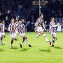 Para pemain Willem II (seragam garis merah-putih-biru) berlari merayakan gol dengan ekspresi gembira di lapangan.