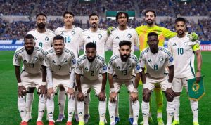 Timnas Arab Saudi berpose formal di lapangan sepak bola dalam formasi tim, mengenakan seragam tandang putih dan hijau.