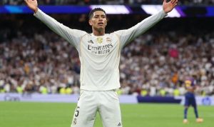 Real-Madrid-Bellingham-Selebrasi-El-Clasico-Sikat-Barcelona.webp Pemain Real Madrid, Jude Bellingham (nomor 5), merayakan gol dengan tangan terangkat lebar di hadapan suporter.