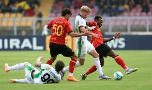 Tiga pemain dari tim dengan jersey merah-kuning dan Sassuolo berebut bola di lapangan, menunjukkan intensitas pertandingan.