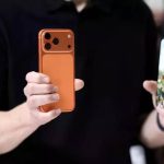 iPhone-17-Penjualan-Fantastis-Model-Baru-Warna-Oranye.webp Dua tangan memegang dua model iPhone terbaru, satu model berwarna oranye dari belakang dan satu model dengan layar menyala menampilkan wajah seorang wanita.