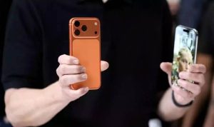 iPhone-17-Penjualan-Fantastis-Model-Baru-Warna-Oranye.webp Dua tangan memegang dua model iPhone terbaru, satu model berwarna oranye dari belakang dan satu model dengan layar menyala menampilkan wajah seorang wanita.