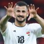 Aymen Hussein pemain sepak bola Timnas Irak dengan jersey putih dan nomor punggung 18, tersenyum dan mengangkat kedua tangannya seolah menyapa atau merayakan