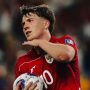pemain tim nasional sepak bola Indonesia, Ole Romeny berambut cokelat muda, mengenakan jersey merah dengan logo Garuda dan nomor punggung 10, sedang memegang bola di lapangan dengan ekspresi serius dan fokus.
