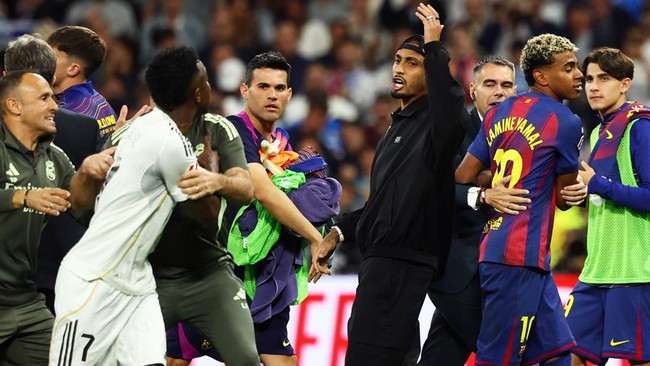 Vinicius-Junior-Ketegangan-El-Clasico-Courtois-Lamine-Yamal.jpg Vinicius Junior berdebat dengan pemain Barcelona di El Clasico, dengan Courtois dan Lamine Yamal terlihat di latar belakang, memicu ketegangan di lapangan.