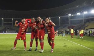 Pemain Persija Jakarta (kostum merah) sedang merayakan gol atau kemenangan, menunjukkan semangat juang dan kebersamaan.