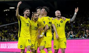 Perayaan-Pemain-Sepakbola-Malaysia-Ancaman-FIFA.jpg Sekelompok pemain sepak bola Malaysia (atau tim berseragam kuning) merayakan gol dengan ekspresi gembira dan tangan terangkat di hadapan tribun penonton yang penuh.