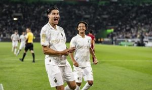 kevin-diks-gol-perdana-borussia-monchengladbach-rating-tinggi.jpeg Pemain Borussia Monchengladbach (jersey putih) merayakan gol dengan teriakan gembira di lapangan, didukung oleh rekan setim di belakangnya, menunjukkan emosi kemenangan.