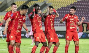 Pemain Persija Jakarta (berbaju merah oranye) sedang menggiring bola dengan fokus di lapangan saat malam hari.