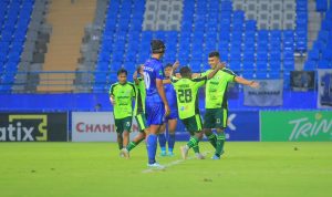 Pemain Persiba Balikpapan (biru kuning) berlari mengejar bola dalam pertandingan sepak bola, dengan fokus pada aksi di lapangan.