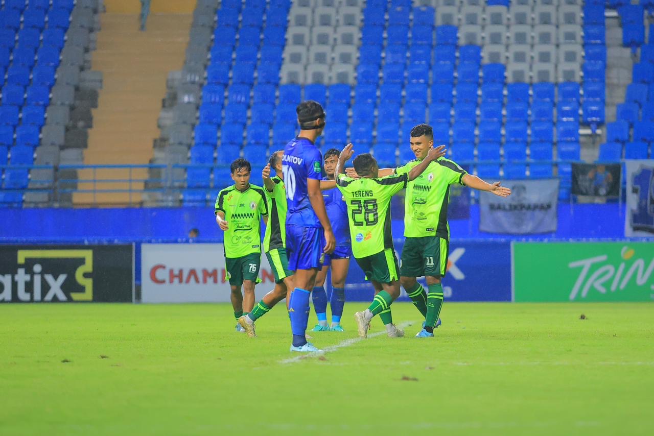 Pemain Persiba Balikpapan (biru kuning) berlari mengejar bola dalam pertandingan sepak bola, dengan fokus pada aksi di lapangan.