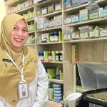 Potret Dwi Siswati di area farmasi Puskesmas Margo Mulyo, seorang tenaga ahli yang mengabdi di dunia farmasi.