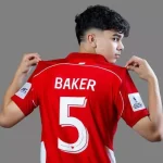 Pemain muda Timnas U-17 Indonesia (bernama BAKER) memegang kerah jersey merah dengan nomor punggung 5 yang besar.