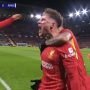 Pemain Liverpool berseragam merah merayakan gol dengan teriakan kegembiraan, memeluk rekan setim di lapangan, menunjukkan skor "LIV 1-0 RMA" di papan skor.