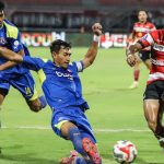 Pemain Madura United dengan jersey merah putih mencoba mengadang pergerakan pemain Arema FC dalam duel sengit di tengah lapangan.