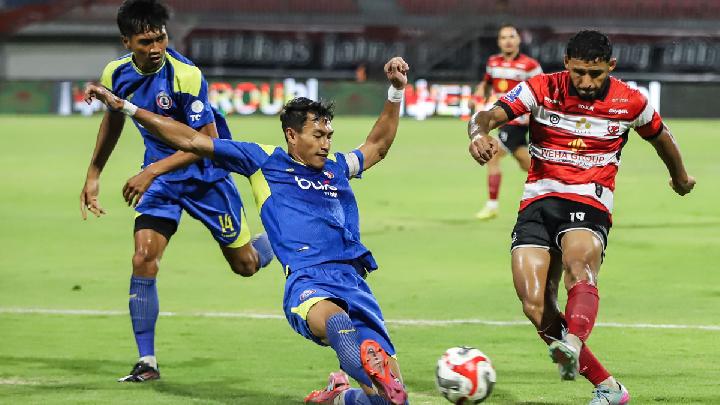 Pemain Madura United dengan jersey merah putih mencoba mengadang pergerakan pemain Arema FC dalam duel sengit di tengah lapangan.
