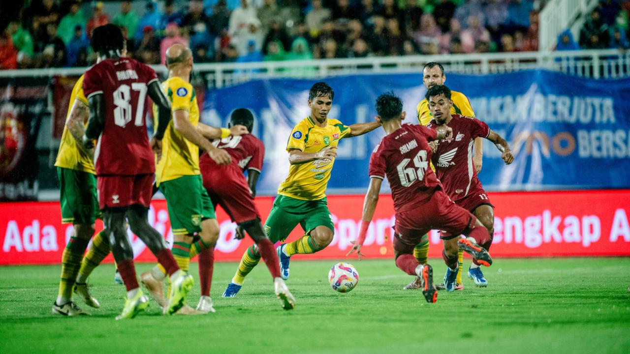 Pemain Persebaya sedang menggiring bola melewati hadangan ketat pemain PSM Makassar dalam pertandingan Liga 1.