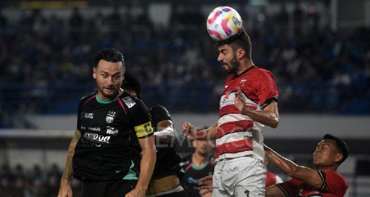 Pemain Persib Bandung berduel memperebutkan bola dengan pemain Madura United di tengah lapangan saat cuaca hujan.