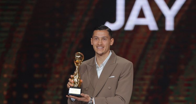 Jay Idzes tersenyum memegang trofi penghargaan di panggung PSSI Awards 2026 dengan latar belakang tulisan JAY.