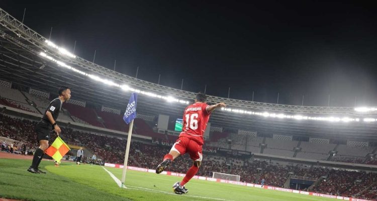 Dony Tri Pamungkas mengambil tendangan sudut dalam pertandingan Timnas Indonesia di stadion megah, dengan hakim garis melihat dari dekat.