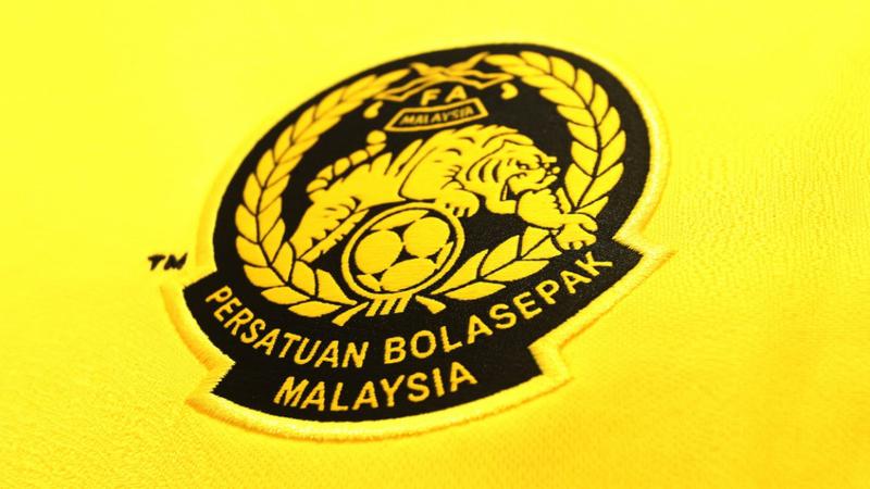 Close-up logo resmi Persatuan Bolasepak Malaysia (FAM) yang tersemat pada jersey kuning, berkaitan dengan tuntutan penjelasan sanksi AFC.