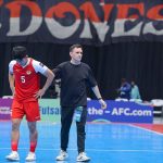 Pemain nomor 5 dan pelatih Timnas Futsal Indonesia di AFF Futsal 2026 sedang berada di lapangan dengan latar belakang bendera merah putih.