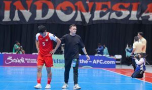 Pemain nomor 5 dan pelatih Timnas Futsal Indonesia di AFF Futsal 2026 sedang berada di lapangan dengan latar belakang bendera merah putih.