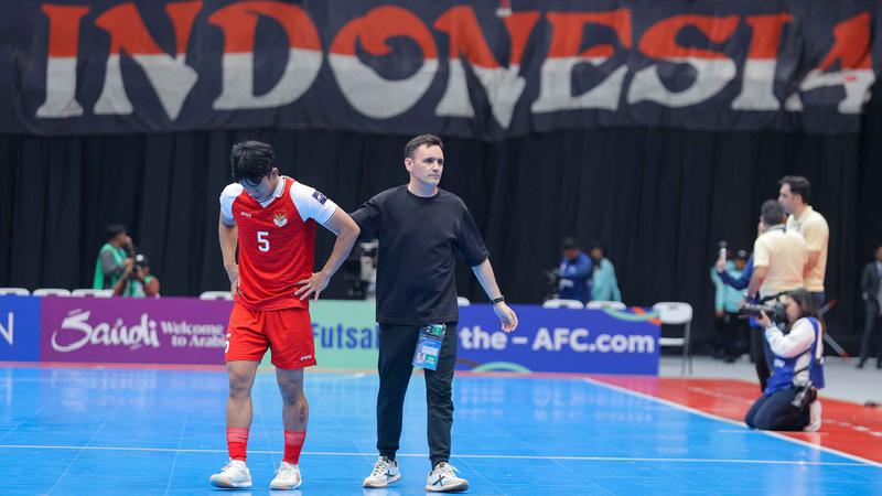 Pemain nomor 5 dan pelatih Timnas Futsal Indonesia di AFF Futsal 2026 sedang berada di lapangan dengan latar belakang bendera merah putih.