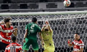 Kiper Madura United menghalau bola di udara saat ditekan pemain Persebaya Surabaya dalam laga Derbi Suramadu di Stadion Gelora Bung Tomo.