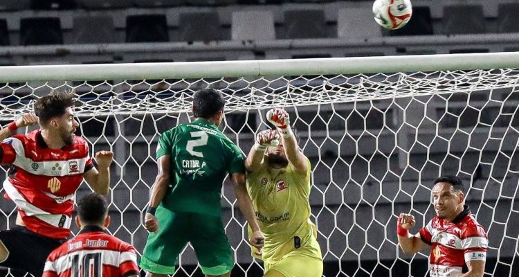 Kiper Madura United menghalau bola di udara saat ditekan pemain Persebaya Surabaya dalam laga Derbi Suramadu di Stadion Gelora Bung Tomo.