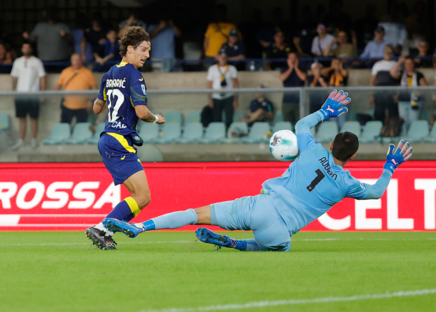 Emil Audero melakukan penyelamatan akrobatik dengan menepis bola saat berhadapan satu lawan satu dengan pemain lawan, memperlihatkan komitmennya untuk menghindarkan tim dari degradasi.