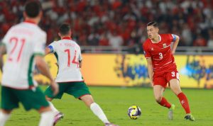 Jay Idzes saat mengontrol bola dalam pertandingan Timnas Indonesia menggunakan jersey merah bernomor punggung 3.
