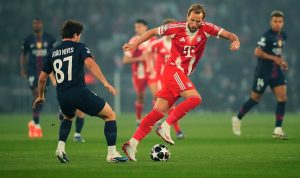 Harry Kane dari Bayern München sedang mendribel bola melewati pemain PSG João Neves dalam pertandingan Liga Champions di Allianz Arena.