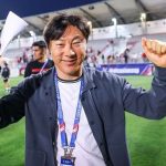 Pelatih Shin Tae-yong tersenyum ramah sambil mengepalkan tangan di area stadion sepak bola. Persija Jakarta