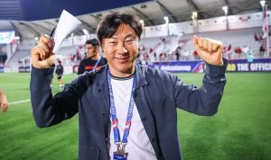 Pelatih Shin Tae-yong tersenyum ramah sambil mengepalkan tangan di area stadion sepak bola. Persija Jakarta