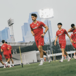 Para pemain Timnas Indonesia mengenakan jersey latihan merah sedang berlari di lapangan sepak bola luar ruangan.