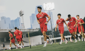 Para pemain Timnas Indonesia mengenakan jersey latihan merah sedang berlari di lapangan sepak bola luar ruangan.