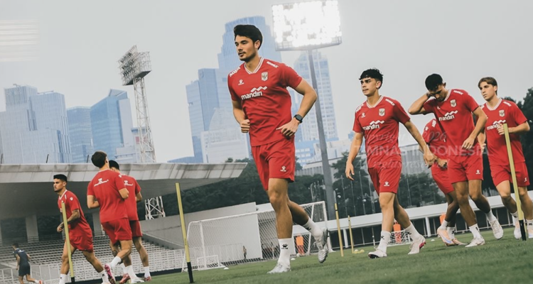 Para pemain Timnas Indonesia mengenakan jersey latihan merah sedang berlari di lapangan sepak bola luar ruangan.