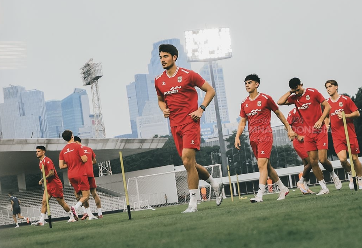 Para pemain Timnas Indonesia mengenakan jersey latihan merah sedang berlari di lapangan sepak bola luar ruangan.